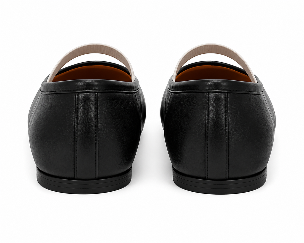 A pair of black leather slip-on shoes shown from the back, featuring a smooth leather upper, a light beige strap, and a black sole, set against a plain white background.