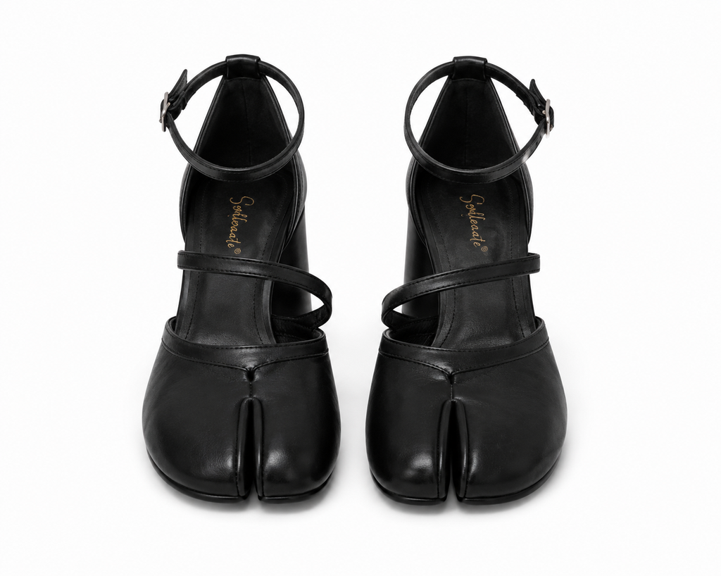 A pair of black leather Tabi-style high heels with ankle straps and a split toe, shown from the front on a white background. The brand name 'Satchi' is printed in gold on the insole of each shoe.